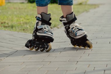 Koruyucu ekipman ve patenler içinde küçük bir çocuk parkta yürüyüş yolunda duruyor, alçak açılı.