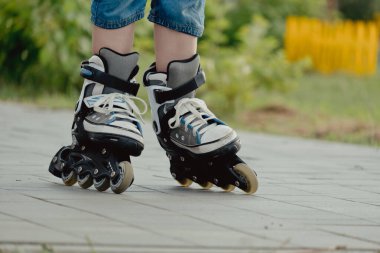 Koruyucu ekipman ve patenler içinde küçük bir çocuk parkta yürüyüş yolunda duruyor, alçak açılı.