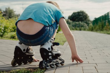 Koruyucu ekipman ve patenler içinde küçük bir çocuk parkta yürüyüş yolunda duruyor, alçak açılı.