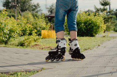 Koruyucu ekipman ve patenler içinde küçük bir çocuk parkta yürüyüş yolunda duruyor, alçak açılı.