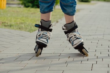 Koruyucu ekipman ve patenler içinde küçük bir çocuk parkta yürüyüş yolunda duruyor, alçak açılı.