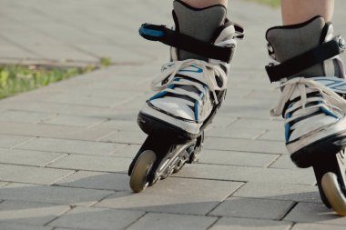 Koruyucu ekipman ve patenler içinde küçük bir çocuk parkta yürüyüş yolunda duruyor, alçak açılı.