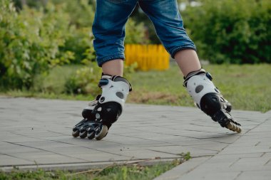 Koruyucu ekipman ve patenler içinde küçük bir çocuk parkta yürüyüş yolunda duruyor, alçak açılı.