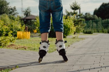 Koruyucu ekipman ve patenler içinde küçük bir çocuk parkta yürüyüş yolunda duruyor, alçak açılı.