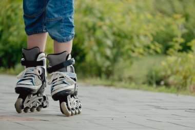 Koruyucu ekipman ve patenler içinde küçük bir çocuk parkta yürüyüş yolunda duruyor, alçak açılı.