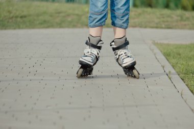 Koruyucu ekipman ve patenler içinde küçük bir çocuk parkta yürüyüş yolunda duruyor, alçak açılı.