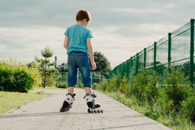 Koruyucu ekipman ve patenler içinde küçük bir çocuk parkta yürüyüş yolunda duruyor, alçak açılı.