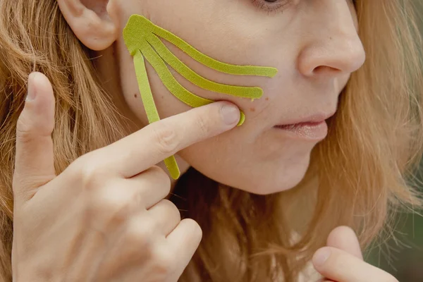 Young woman with green tapes on face. Face aesthetic taping. Attractive young woman with kinesiology tapes on forehead. Beautiful Woman With Kinesiology Facelift Tapes