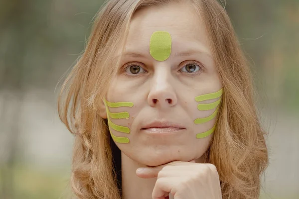 Young woman with green tapes on face. Face aesthetic taping. Attractive young woman with kinesiology tapes on forehead. Beautiful Woman With Kinesiology Facelift Tapes