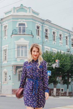 Bahar caddesinde yürüyen mavi elbiseli, yuvarlak çantalı güzel bir kadın. Şehir geçmişi. Şık bir turist kız hafta sonu gezisi boyunca şehirde gezmekten zevk alıyor..