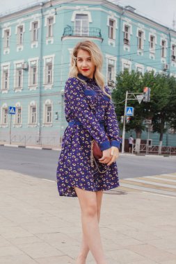 Bahar caddesinde yürüyen mavi elbiseli, yuvarlak çantalı güzel bir kadın. Şehir geçmişi. Şık bir turist kız hafta sonu gezisi boyunca şehirde gezmekten zevk alıyor..