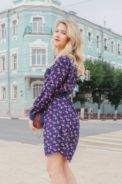 Bahar caddesinde yürüyen mavi elbiseli, yuvarlak çantalı güzel bir kadın. Şehir geçmişi. Şık bir turist kız hafta sonu gezisi boyunca şehirde gezmekten zevk alıyor..