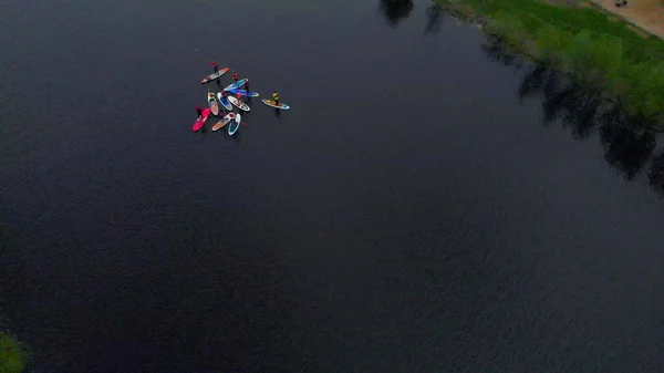 Aerial view group active sports surfer performing supsurfing stranding on surfboard with paddle river water surface. Water sport, supsurfing. Summer holidays vacation travel.