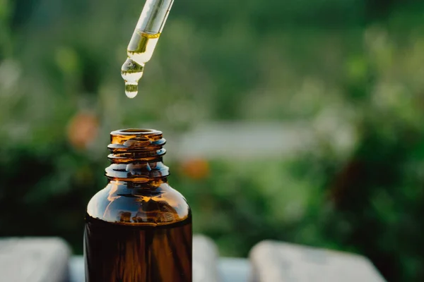 Pipette and bottle of essential oil. Eucalyptus essential oil dripping from pipette into bottle, closeup. Oily drop falls from a cosmetic pipette.