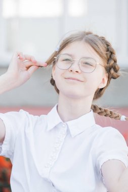 Eğitim kavramı. İlkokulun gözlüklü kız öğrencisi. Üniformalı. Saçlarını örgü yapıp gülümsüyor. Gözlüklü komik kız okula hazır..