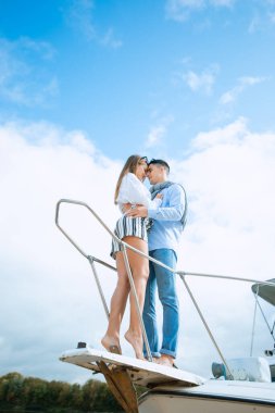 Yelkenlinin güvertesinde sarılan genç çift. Zevk teknesinde romantik bir çift. Mutlu zengin bir adam ve bir kadın özel bir tekneyle deniz seyahati yapıyorlar. Balayında yatla gezen çift.