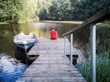 Nehir kıyısındaki ahşap iskelede oturan hayalperest kızın arka manzarası.