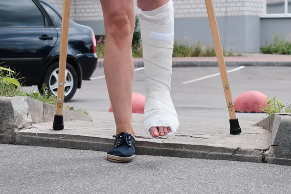 A woman with a broken leg overcomes an obstacle with crutches.