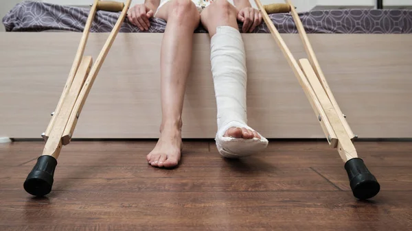Woman with broken leg sitting on the bed and holding crutches. High quality photo