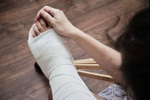 A woman massages the toes of a broken leg with her hands. Top view of a broken leg in a plaster cast and crutches. Home rehabilitation after a broken leg. High quality photo