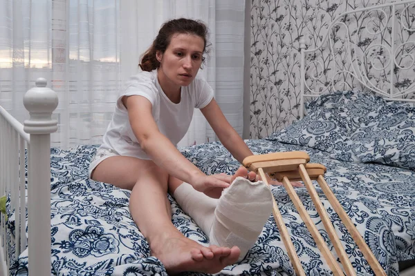 A woman massages the toes of a broken leg with her hands. Top view of a broken leg in a plaster cast and crutches. Home rehabilitation after a broken leg. High quality photo. High quality photo