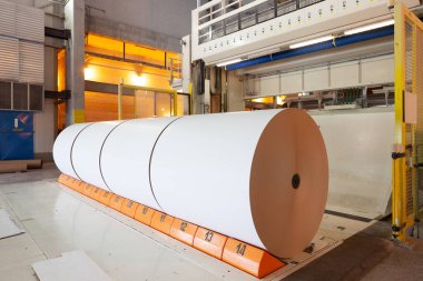 Big rolls of paper coming out of the machinery in a paper mill plant. clipart