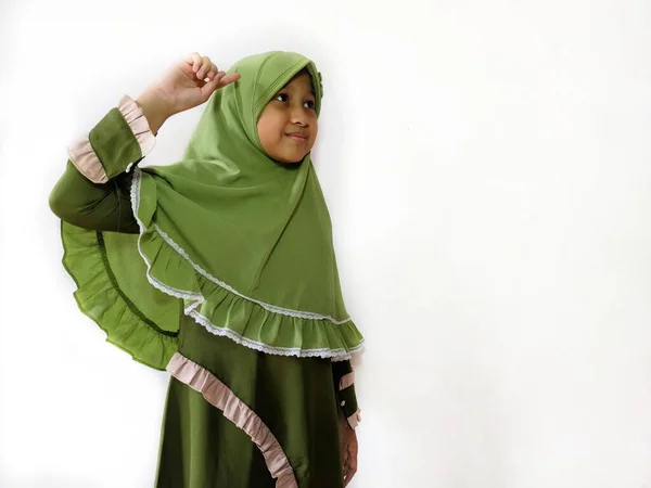 Indonesian Muslim girl making thinking gesture in front of a white background with big smile, wearing green clothes