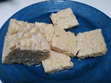 Sabah kızartılmaya hazır tuzlu suyla dolu mavi bir tabakta tempeh dilimleri.