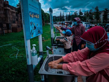 Malang, Endonezya -14 Şubat 2021: Müslüman bir kadın ve iki çocuğu, turistik bir yerden dönmeden önce otoparkın önünde ellerini yıkıyorlar.