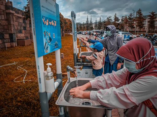 Malang, Endonezya -14 Şubat 2021: Müslüman bir kadın ve iki çocuğu, turistik bir yerden dönmeden önce otoparkın önünde ellerini yıkıyorlar.