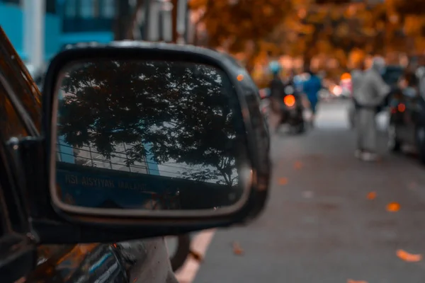Close up photo of a car mirror reflecting the shadow of a building and with a blurred background