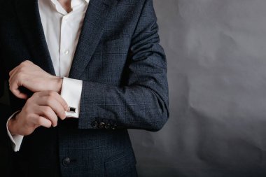 Gri arka planda kol düğmesini tamir eden smokinli bir adamın yakın çekimi. Damat papyonu kol düğmeleri.