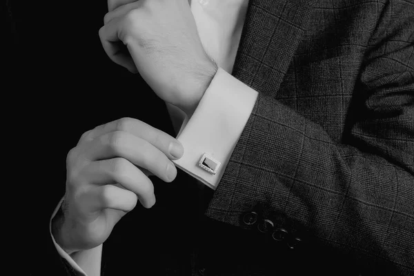 Black and white photo of male hands. Handsome groom dressed in black formal suit, white shirt and tie is getting ready for wedding.