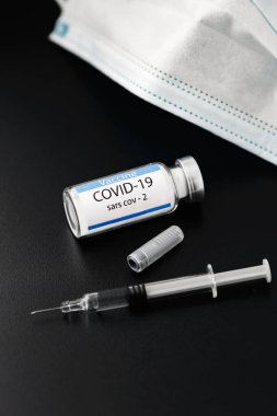 SARS-CoV-2 aşı şişesinin yanında siyah arka planı olan bir şırınga.. 