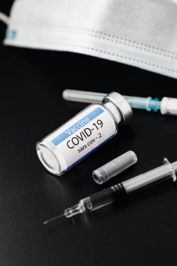 SARS-CoV-2 aşı şişesinin yanında siyah arka planı olan bir şırınga.. 