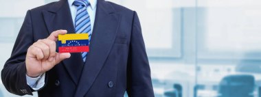 Venezuela 'nın baskılı bayrağıyla plastik kredi kartı tutan işadamının kesilmiş görüntüsü. Arkaplan bulanık.