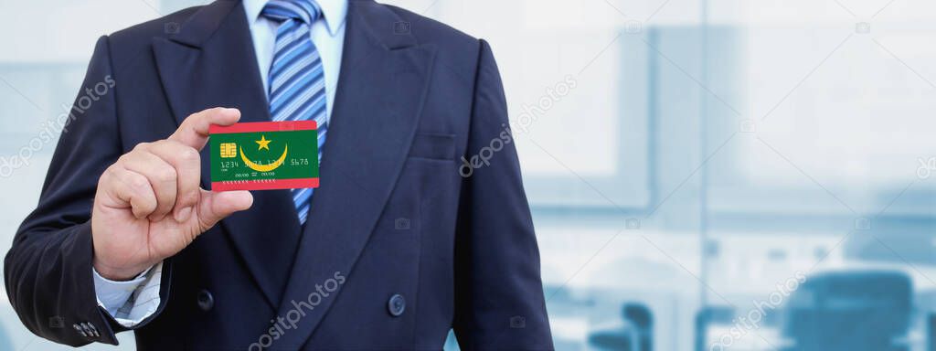 Cropped image of businessman holding plastic credit card with printed flag of Mauritania. Background blurred.