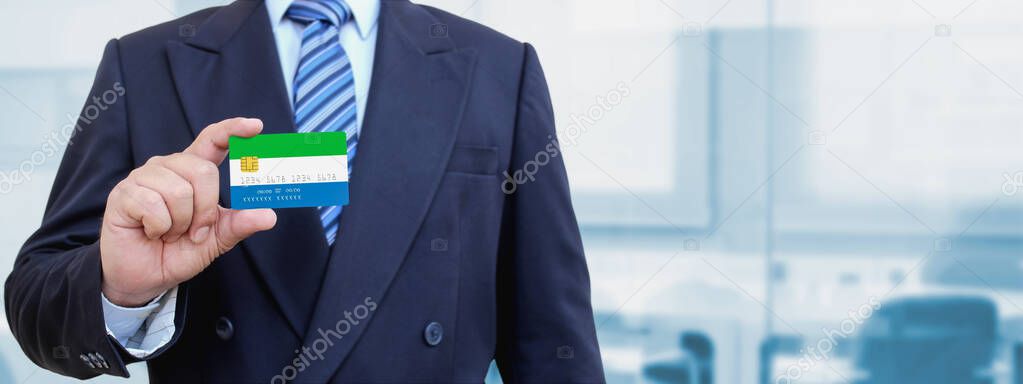 Cropped image of businessman holding plastic credit card with printed flag of Sierra Leone. Background blurred.