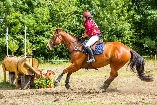 Saint Cyr du Doret, Francia - 29 de julio de 2016: Mujer montando a caballo sobre un obstáculo en un evento a campo traviesa — Foto de Stock