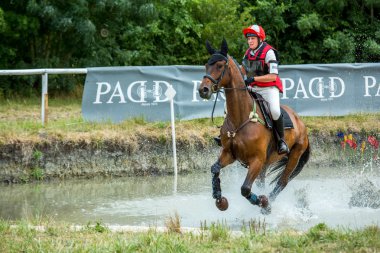 Saint Cyr du Doret, France - July 29, 2016: Rider crossing water jump galloping at a cross country manisfestation clipart