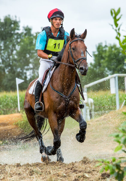 Saint Cyr du Doret, France - July 29, 2016: Rider crossing water jump galloping at a cross country manisfestation