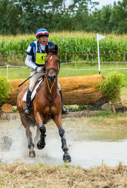 Saint Cyr du Doret, France - July 29, 2016: Rider crossing water jump galloping at a cross country manisfestation