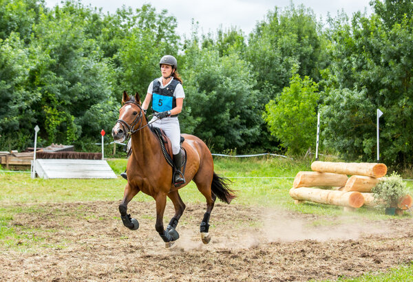Saint Cyr du Doret, France - July 29, 2016: Rider on her galloping horse during a cross country manisfestation