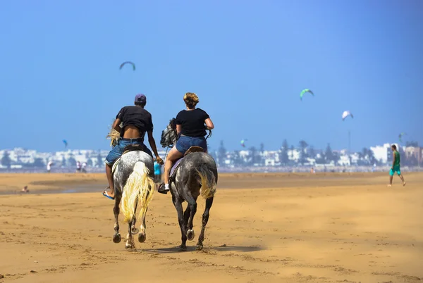 En kvinna och en man som rider på hästryggen längs sandstranden — Stockfoto