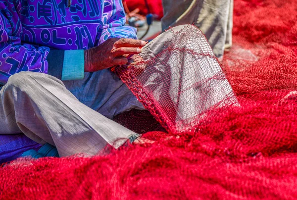 Un primo piano per le mani del pescatore cucire rete da pesca rossa — Foto Stock