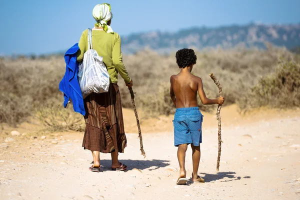 Uma velha e um jovem rapaz a caminhar pela estrada empoeirada — Fotografia de Stock