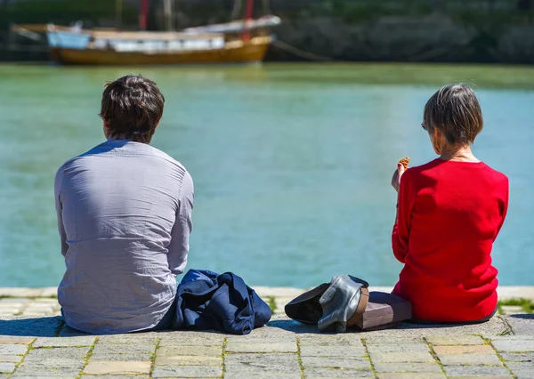 Um homem e uma mulher sentados no cais e a olhar para o mar — Fotografia de Stock