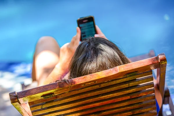 Fechar a jovem mulher mensagens de texto em seu telefone celular enquanto relaxa na piscina — Fotografia de Stock