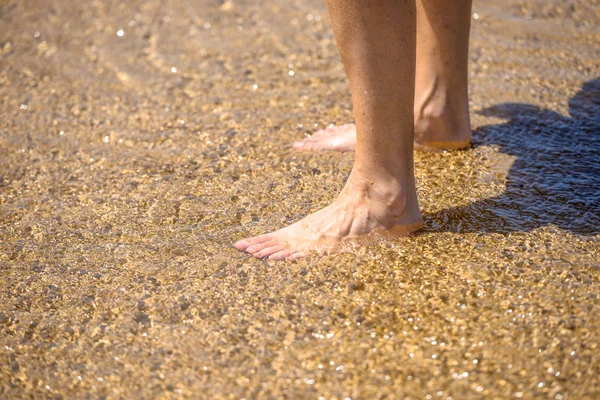 Un par de piernas de pie sobre la arena suave en la playa en el sol — Foto de Stock