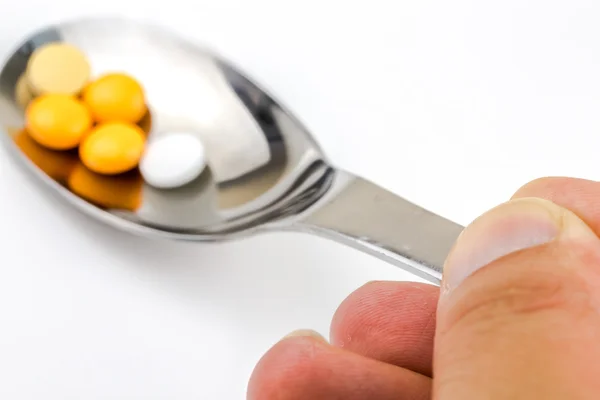 Tenant une cuillère avec des pilules médicales sur fond blanc — Photo